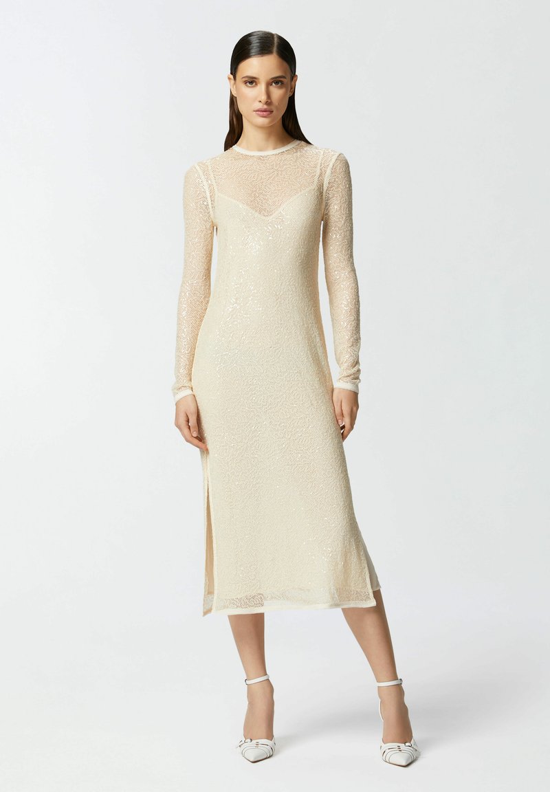 Haljina dugih rukava kremaste boje s uskim korzetom, prozirnim prekrivačem, suptilnim sjajem i bočnim prorezom. Izrađena od nježne, teksturirane tkanine.