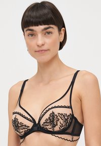 Μαύρο σουτιέν από δαντέλα με λουλουδάτη κεντηση σε διάφανο δίχτυ με κυρτές άκρες και ρυθμιζόμενους ιμάντες. Περιλαμβάνει στήριξη με μπάντα.