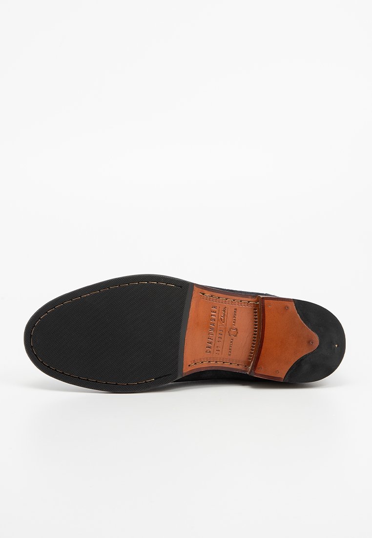 Lederschuhsohle mit schwarzem Gummiunterboden und braunem Lederinnenfutter, mit einer Naht entlang der Kante und einem eingeprägten Logo-Detail.