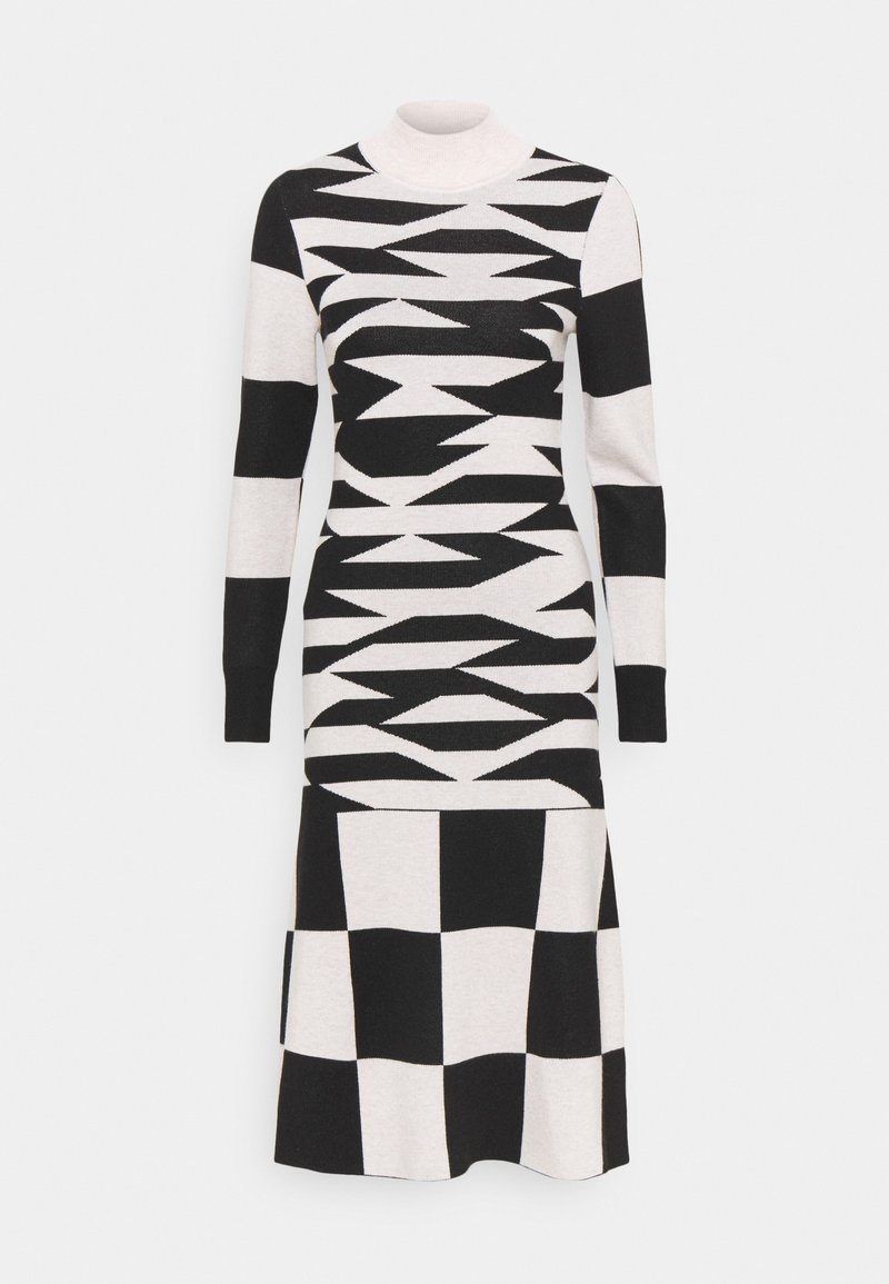 Robe en maille à manches longues présentant des motifs géométriques noirs et blancs, comprenant des zigzags et des motifs à carreaux, avec un col montant simulé.