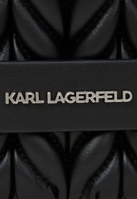 Zwarte, gewatteerde leren handtas met een zilveren "KARL LAGERFELD" logo en een gladde contrasterende band. De gestructureerde afwerking voegt diepte toe.