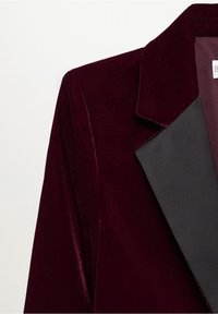 Bordeauxrode fluwelen blazer met een contrasterende zwarte satijnen revers. Voorzien van een scherpe kraag en een gladde textuur, die het op maat gemaakte ontwerp benadrukken.
