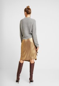 Grå stickad tröja, metallisk gyllene kjol med draperad design och knähöga bordeauxfärgade stövlar. Texturerade material och livliga färger.