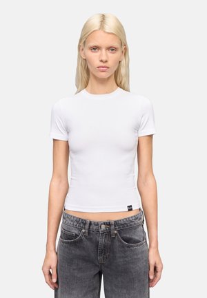 Camiseta blanca de manga corta ajustada con cuello redondo, hecha de una tela elástica, combinada con unos jeans de talle alto gris oscuro que tienen bolsillos frontales.