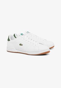 Witte leren sneakers met groene hielaccenten, voorzien van een textuur, rubberen zool en een geborduurd krokodil-logo aan de zijkant.