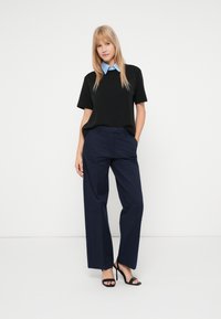 Černé tričko s krátkým rukávem a světle modrým límcem, doplněné tmavě modrými kalhotami širokého střihu a černými jehlovými podpatky.