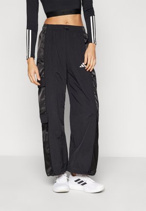 Person wearing black wide-leg cargo pants with side pockets, black crop top with white stripes on sleeves, and white sneakers with black stripes.