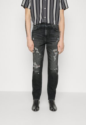 Jeans de mezclilla negra con corte ajustado, con detalles desgastados y parches deshilachados. Combinado con una camisa de rayas de manga corta y botas negras.