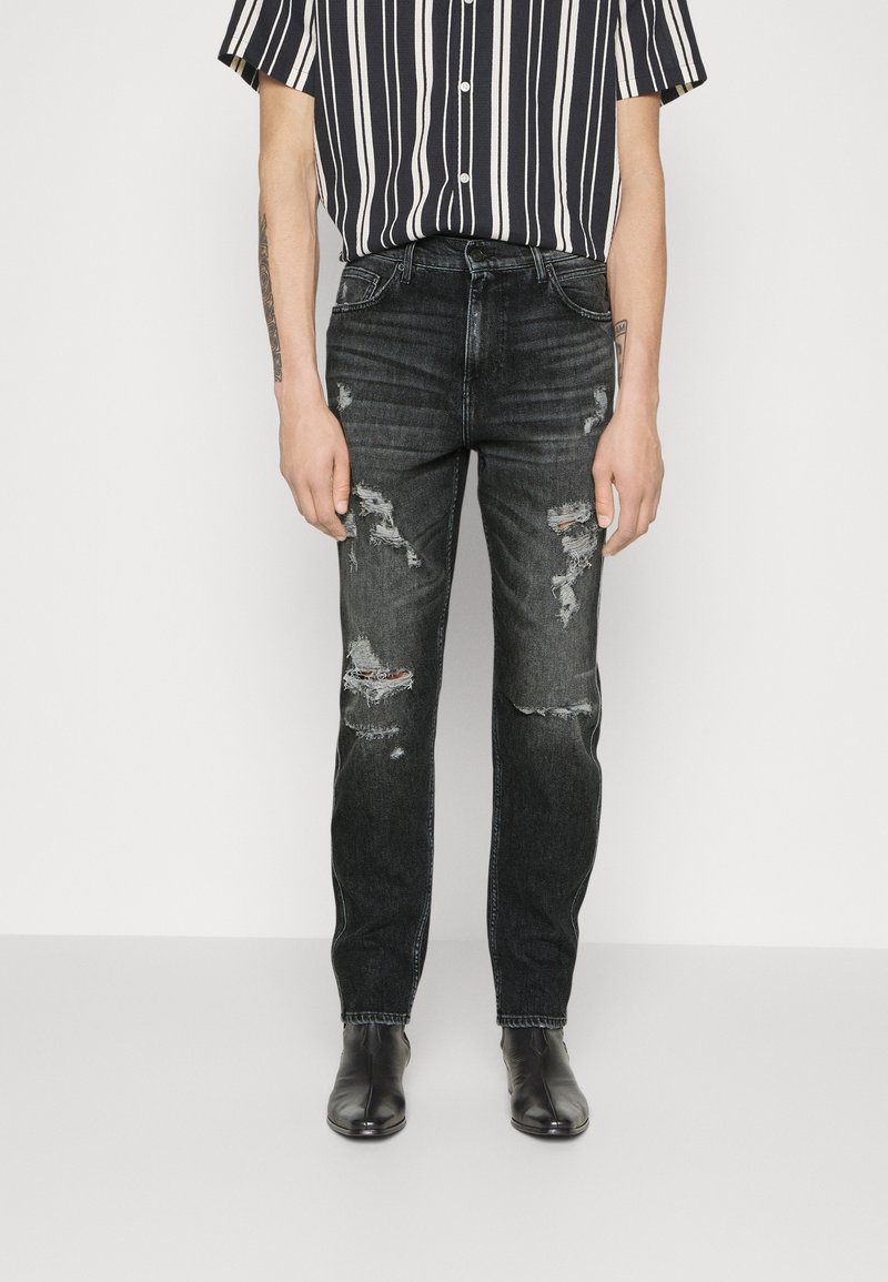 Musta farkut slim fit -leikkauksella, joissa on kuluneita yksityiskohtia ja revittyjä kohtia. Yhdistettynä lyhythihaiseen, raidalliseen paitaan ja mustiin saappaisiin.