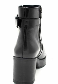 Stivaletto alla caviglia in finta pelle nera con tacco spesso, zip laterale e cinturino regolabile con fibbia. Texture liscia e design elegante.