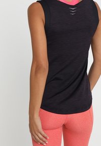 Mustat urheilutoppi tekstiilikuosilla, jossa on pyöreä pääntie ja kolme pientä halkiota selässä. Yhdistetty kirkkaanpinkkeihin legginsseihin.