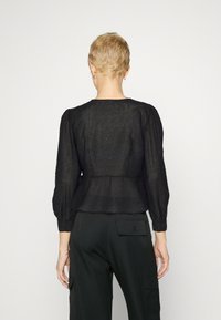 Blusa nera texturizzata con maniche lunghe a sbuffo e vita cintrata. Caratterizzata da una leggera lucentezza e da un collo rotondo. Abbinata a pantaloni scuri.