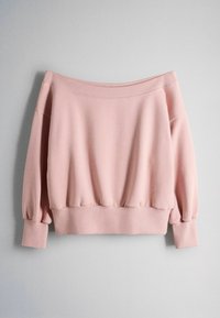 Zachtroze off-shoulder sweatshirt met lange mouwen en geribde boorden, zoom en halslijn tegen een eenvoudige lichte achtergrond.