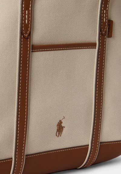 Sac en toile beige avec des sangles et finitions en cuir marron, doté d'un petit logo brodé de joueur de polo près du bas au centre.