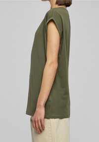 Olivově zelené tričko s krátkým rukávem vyrobené z měkké bavlny, s uvolněným střihem, kulatým výstřihem a ohrnutými rukávy, zakončené rovním lemem.