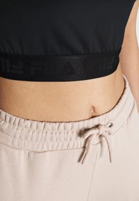 Černý zkrácený top s texturovaným logem, spárovaný se světlými béžovými teplákovými kalhotami s šňůrkou a nařaseným pasem.
