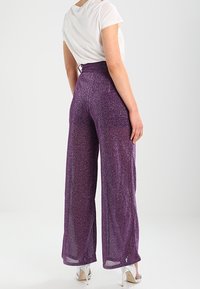 Purple wide-leg trousers made of a shiny, textured fabric; elastic waistband; sheer material; paired with a white top and silver heels.