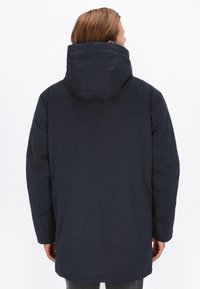 Mørkeblå parka med en stor hætte, der har en glat tekstur og en lige pasform. Den har lange ærmer og en detalje med slids bagpå.