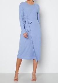 Robe midi à manches longues côtelées en bleu clair avec un design enveloppant et un lien à la taille. Assortie à des sandales à talons blocs transparents.