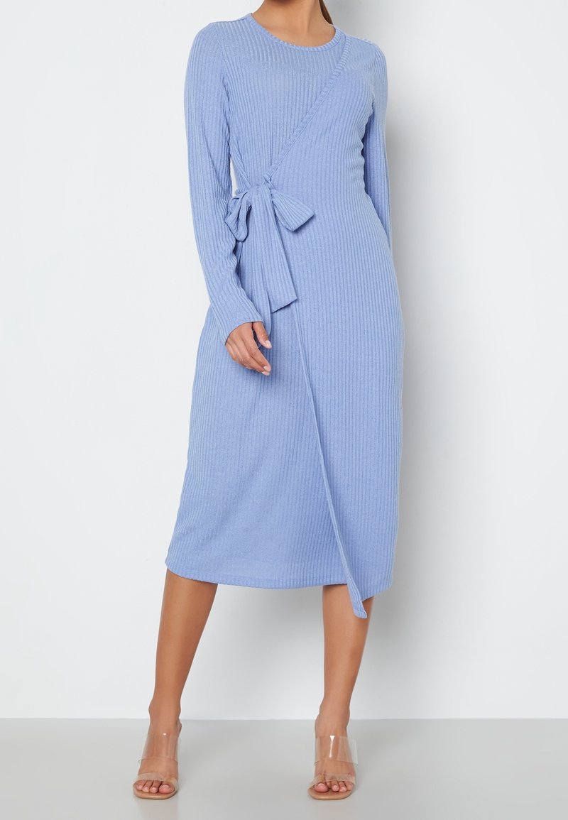 Robe midi à manches longues côtelées en bleu clair avec un design enveloppant et un lien à la taille. Assortie à des sandales à talons blocs transparents.