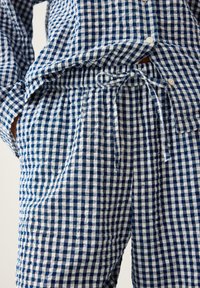 Niebieskie i białe w kratkę spodnie piżamowe z elastycznym pasem i sznurkiem, zestawione z pasującą, kraciastą koszulą z guzikami.