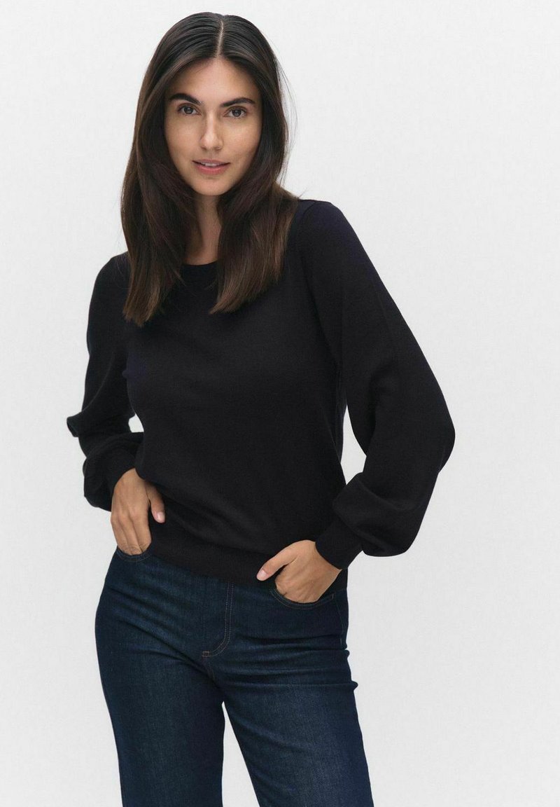 Svart långärmad tröja med rund halsringning; har puffärmar och ribbade muddar. Bärs med mörkblå jeans. Slät textur.