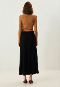 Brun ribbet sweater, sort plisseret maxiskirt, bagansigt. Glat tekstur, tætsiddende foroven, flydende forneden med en bred kant.