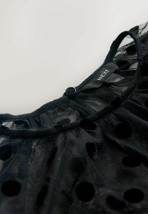 Černý síťovaný top s kulatým výstřihem, sametovým puntíkovým vzorem a knoflíkovým zapínáním na zadní straně. Etiketa nese nápis "NEXT."