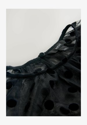 Černý síťovaný top s kulatým výstřihem, sametovým puntíkovým vzorem a knoflíkovým zapínáním na zadní straně. Etiketa nese nápis "NEXT."