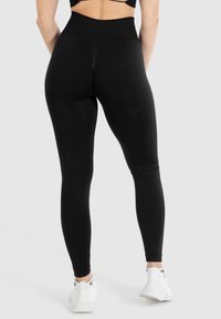Svarta högmidjade leggings med en slät textur, kroppsnära form och ankel-lång design, kombinerade med vita träningsskor.