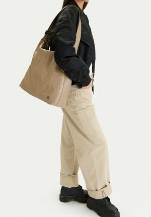 Osoba nosící černou bundu, béžové kalhoty s širokými nohavicemi, černé boty, na pravém rameni velká taupe kožená kabelka.