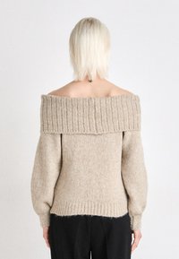 Beige off-shoulder tröja med ribbad krage och långa puffärmar. Mjuk textur, åtsittande nedanför den ribbade nederdelen, lätt stickad.