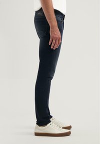 Slim-fit tmavě modré džíny s mírným vyblednutím, se pěti kapsami, šitými detaily, v kombinaci s bílými teniskami.
