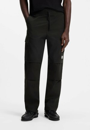 Zwarte cargobroek met zijzakken en een taille met trekkoord, gedragen met zwarte mocassins op een staand persoon.