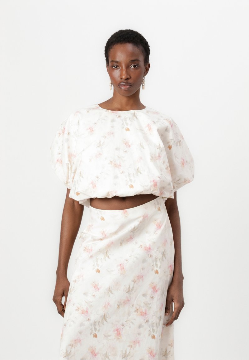 Blomstret sæt bestående af en cropped top med pufærmer og bådudskæring samt en højtaljet nederdel, begge i hvid med pink og grønne mønstre.