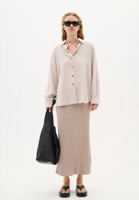Light beige linen button-up shirt, long sleeves, worn with a ribbed beige midi skirt. Black shoulder bag and black sandals complete the outfit.