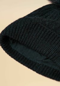 Black knitted beanie with a ribbed texture, soft fleece lining, and a fur pom-pom on top. The interior is smooth and dark.