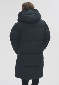 Párnázott fekete parka nagy kapucnival, vízszintes varrással és középhosszú fazonnal. Simább tapintású, melegen szigetelt kabát.