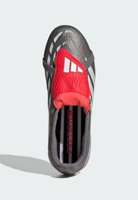 Zapatilla deportiva en negro y gris con acentos rojos, parte superior con patrón, tres franjas blancas y punta texturizada. Interior acolchado con logo impreso.