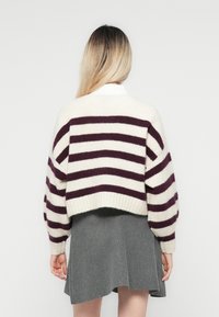 Gekort sweater met brede kastanjebruine en crèmekleurige strepen, gebreide textuur en ribbelmanchetten, gecombineerd met een grijze flared rok.