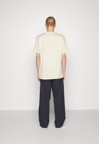 Camiseta de algodón crema de manga corta, combinada con pantalones holgados de color navy. Diseño sencillo con corte recto y sin patrones visibles.