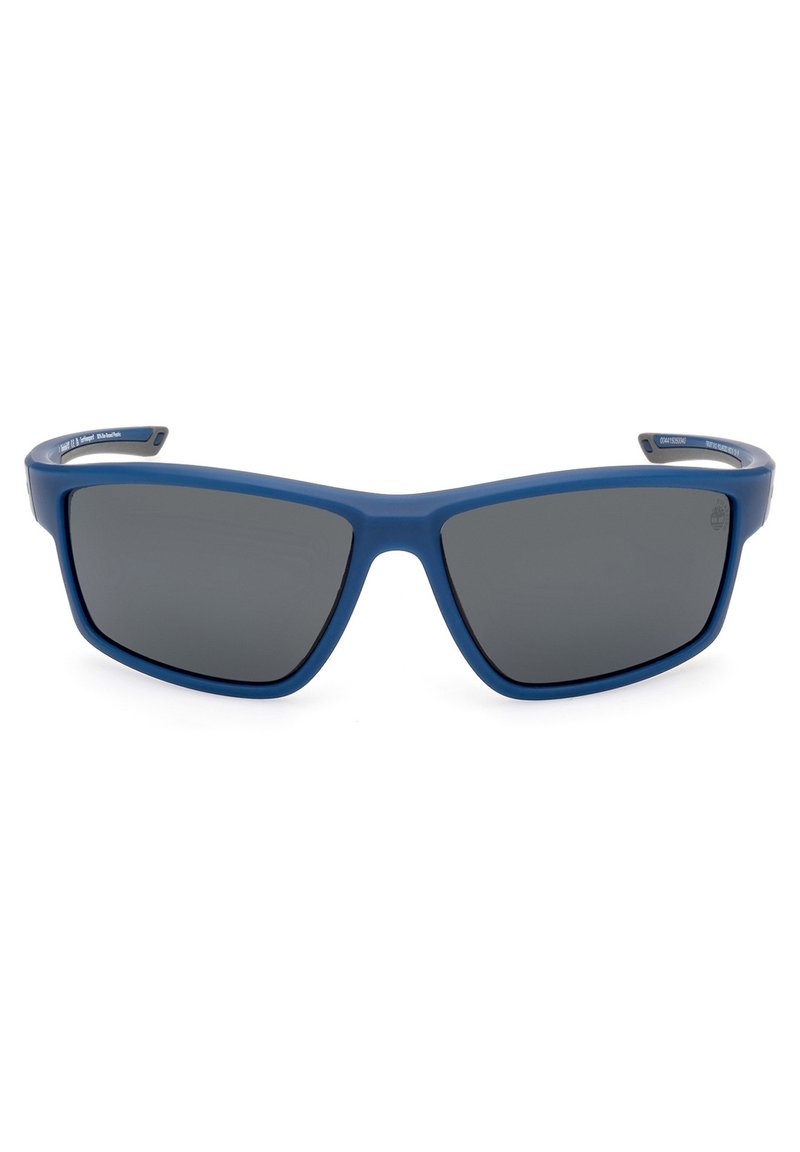 Gafas de sol de plástico azul con forma angular, lentes gris oscuro y acabado texturizado en las varillas. Presenta un logo en una de las varillas.