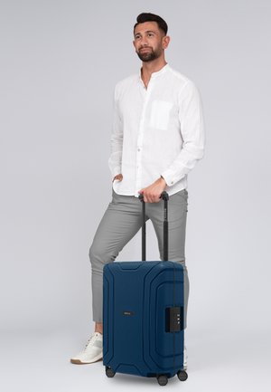 Maleta rígida de color navy con superficie texturizada, detalles con textura y candado de combinación. Cuatro ruedas negras y un asa extensible para mayor movilidad.