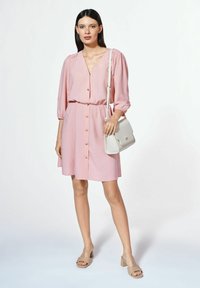 Różowa sukienka z guzikami, z bufiastymi rękawami i ściśniętym w talii fasonem. Połączona z beżową torebką typu crossbody i taupe sandałami na słupku.