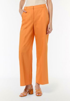 Orange wide-leg trousers made of smooth fabric with front pockets, belt loops, and a tailored fit. Worn with strappy orange heeled sandals.