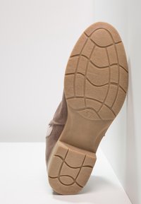 Semelle d'une chaussure brun tan reposant contre un coin blanc, montrant la taille 37 et le motif de la bande de roulement sur la semelle.