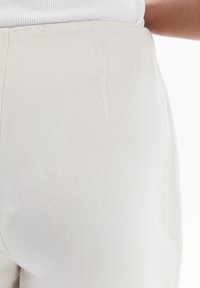Pantalones de color beige claro, de cintura alta, fabricados con un tejido texturizado. Presentan un diseño limpio con un sutil detalle de costura en la parte posterior.