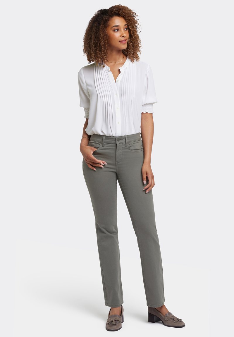 Blusa blanca con pliegues verticales, mangas cortas y botones delanteros, combinada con pantalones rectos grises y zapatos grises con acentos de borlas.