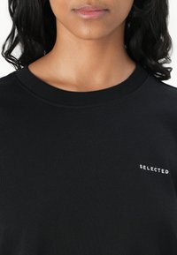 T-shirt in cotone nero con scollo rotondo e maniche corte, con il testo "SELECTED" ricamato in bianco sul petto.