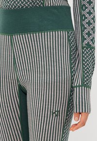 Leggings a rayas verdes y grises con una cinturilla alta, que presentan patrones intrincados y detalles texturizados, fabricados con un tejido elástico.